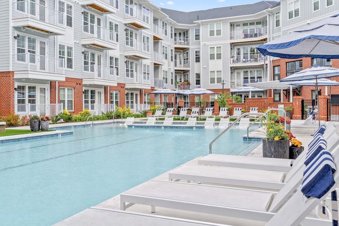 Luxurious apartment complex featuring a pristine swimming pool surrounded by elegant loungers, modern architecture, and vibrant gardens.