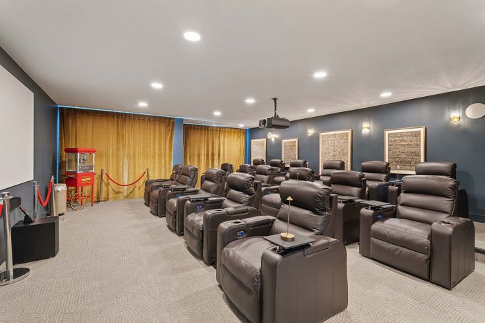 Luxurious home theater with plush recliners, ambient lighting, and a classic popcorn machine against elegant golden curtains.