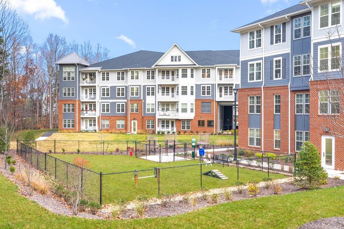 Charming apartment complex with modern architecture, featuring a fenced green play area and patio balconies, nestled in a serene landscape.