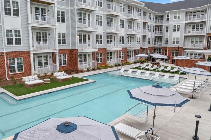 Chic apartment complex featuring a luxurious outdoor pool area with sun loungers and umbrellas, perfect for relaxation and leisure.