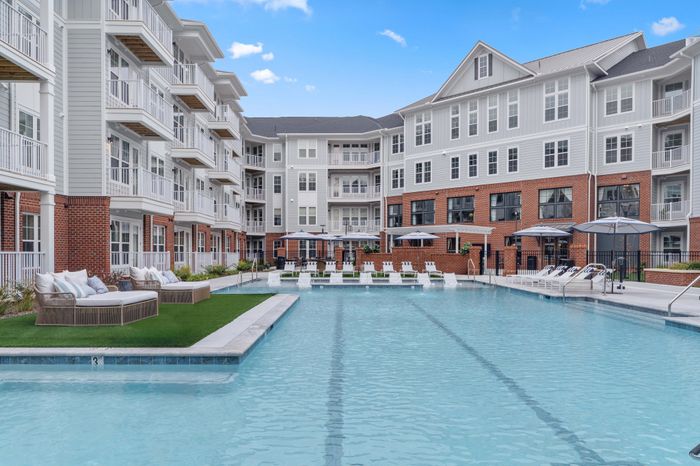 Luxurious apartment complex featuring a sparkling outdoor pool, stylish sun loungers, and chic lounge areas, offering modern elegance and relaxation.