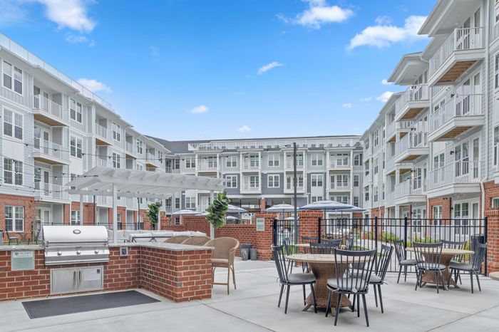Chic apartment courtyard with modern brick and metal finishes, featuring stylish outdoor seating and a built-in grill under a clear blue sky.