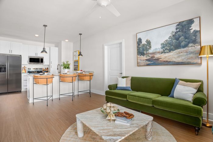 Chic modern living space with an inviting green sofa, stylish artwork, and a sleek kitchen island with rattan bar stools.