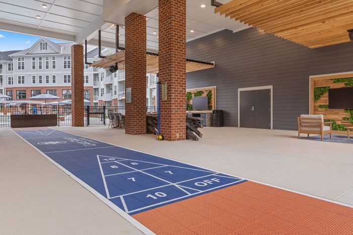 Modern apartment amenity area featuring shuffleboard court, stylish seating, and entertainment spaces with vibrant d&eacute;cor.