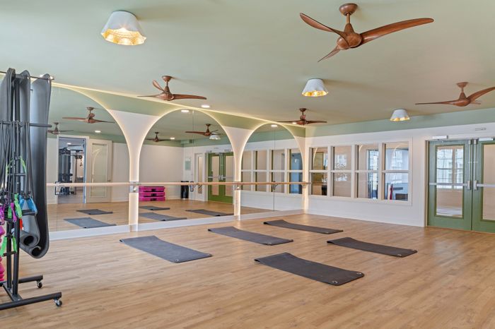 Elegant fitness studio with mirrored walls, yoga mats, and ceiling fans, offering a serene workout environment with modern amenities.