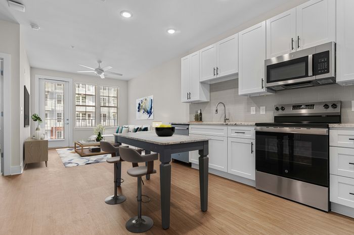 Contemporary apartment kitchen with sleek white cabinets, modern appliances, and a chic dining area leading to a sunlit living space.