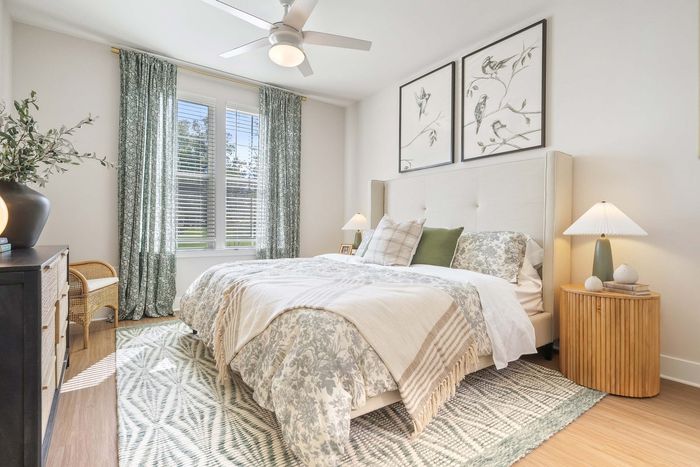 Elegant bedroom with cozy bedding, large windows, and stylish decor, featuring serene artwork and modern lighting.