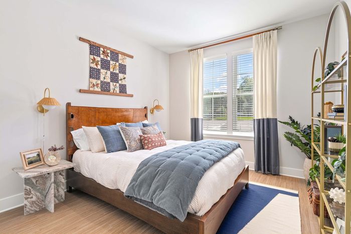 Bright and cozy bedroom featuring a stylish wooden bed with plush pillows, modern decor, and abundant natural light through large windows.