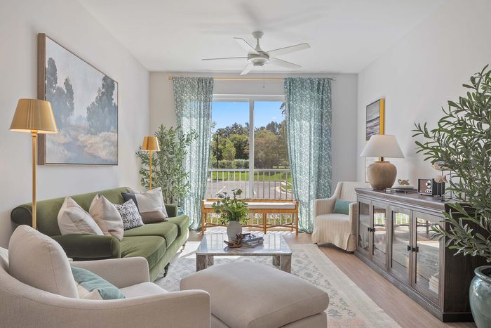 Bright and inviting living room with plush green sofa, cozy chairs, and elegant decor, featuring large windows with serene garden views.