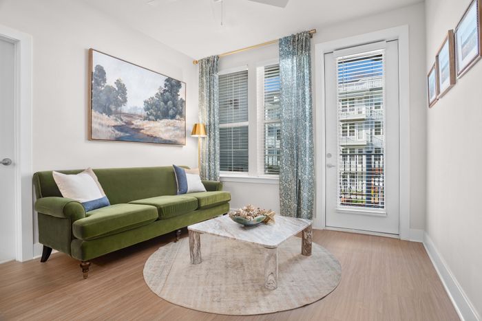 Charming living room with a plush green sofa, elegant artwork, and bright natural light streaming through large windows.