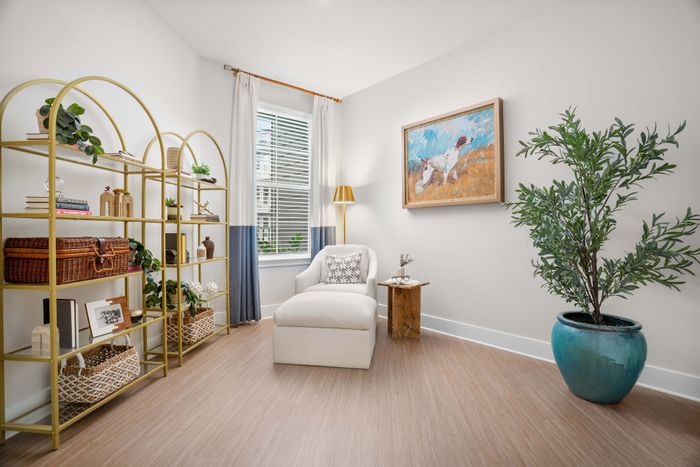 Inviting room with natural light, featuring a cozy white armchair, stylish gold shelving with decorative items, and a vibrant potted plant for a touch of elegance.