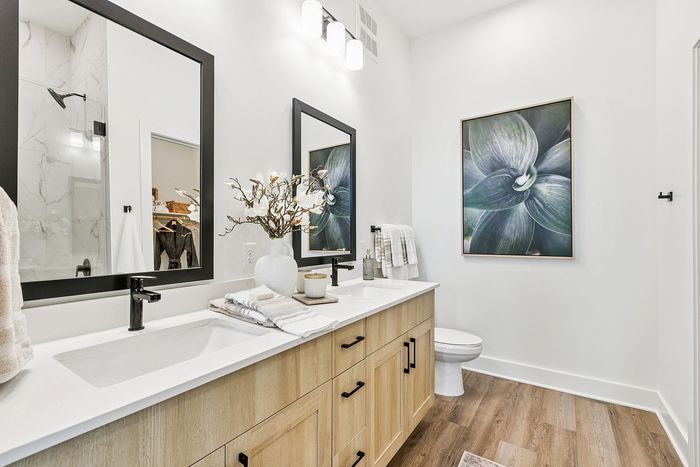 Elegant bathroom with modern double vanity, chic decor, and sleek fixtures, highlighted by stylish wall art and warm wood tones.