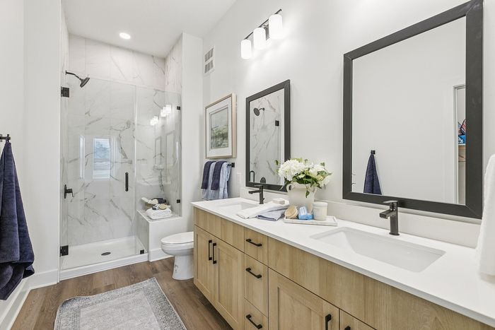 Elegant bathroom with a spacious walk-in shower, modern wood cabinetry, and dual sinks topped with stylish decor and fresh flowers.