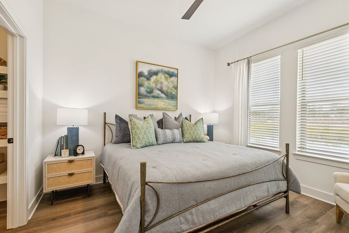 Bright and inviting bedroom with elegant decor, featuring a cozy bed adorned with plush pillows and artwork, enhancing the serene ambiance with natural light streaming through large windows.