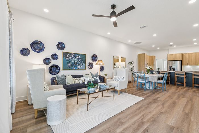 Bright open-concept living and dining area with modern decor, elegant wooden flooring, and stylish kitchen in the background.