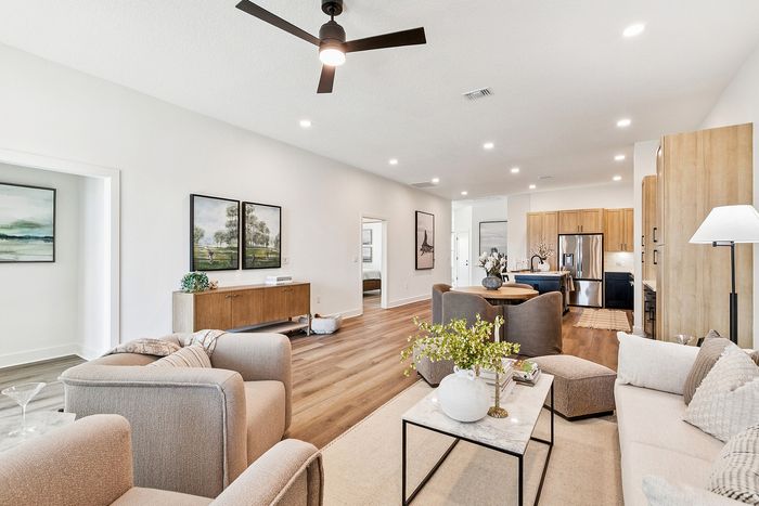 Inviting open-concept living room with elegant furnishing, featuring plush seating, modern art, and a sleek kitchen with wood accents.