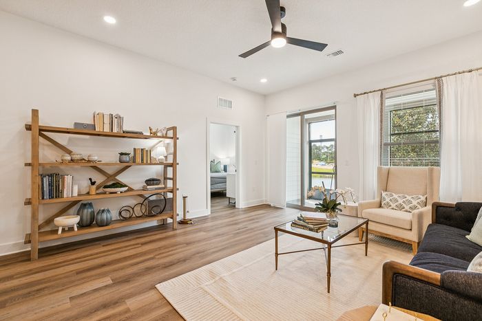 Inviting living room with modern decor, featuring a cozy armchair, elegant bookshelf, and bright natural lighting through large windows.