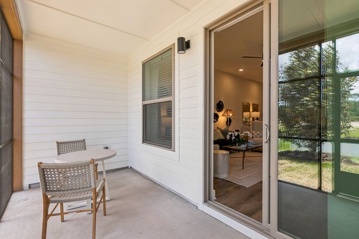 Inviting apartment patio with cozy table and chairs, leading into a stylishly decorated living room with warm lighting and a scenic outdoor view.