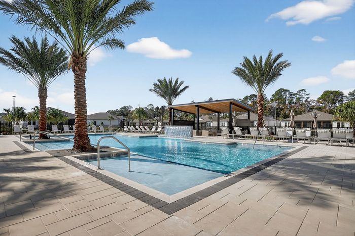 Luxurious outdoor pool with waterfall feature and palm trees, offering a serene resort-like atmosphere.
