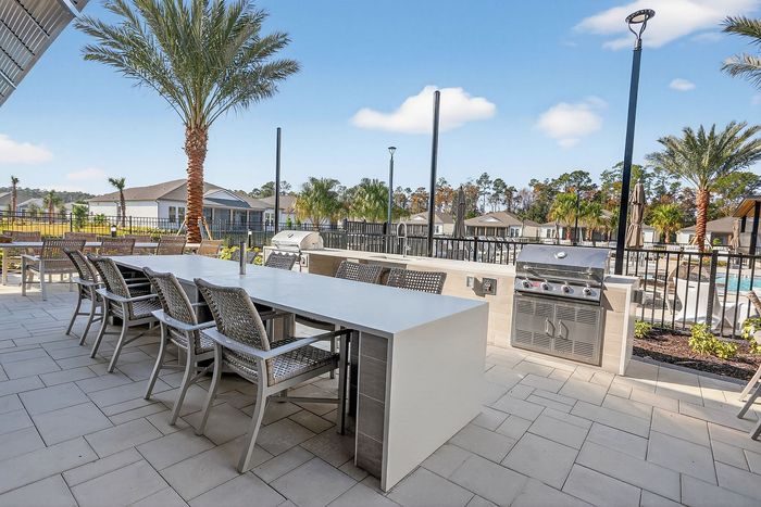 Luxurious outdoor patio with grill, modern seating, and lush palm trees, perfect for entertaining or relaxing in a sunny oasis.