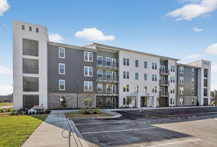 Modern four-story apartment building with sleek design, featuring private balconies and expansive windows, set against a clear blue sky.