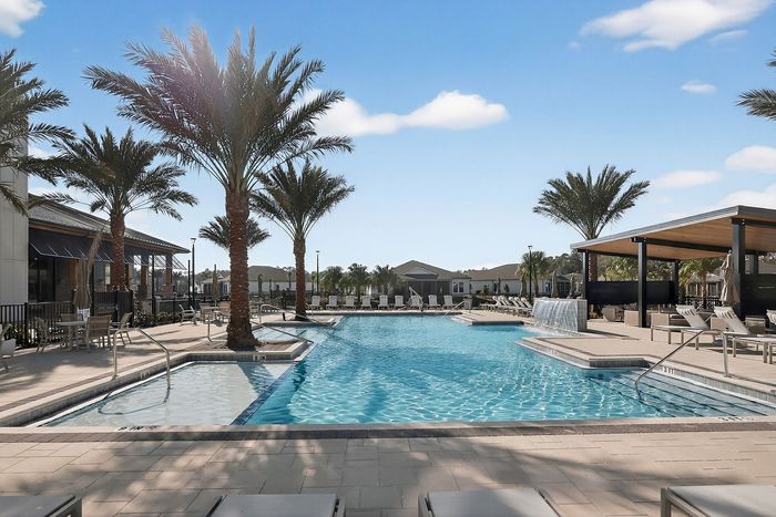 Luxurious outdoor pool area with palm trees, sun loungers, and a modern cabana under a bright blue sky.
