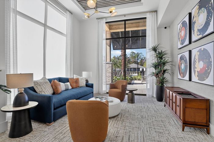 Modern living room with large windows, vibrant blue sofa, accent chairs, stylish decor, and lush greenery offering a bright and inviting atmosphere.
