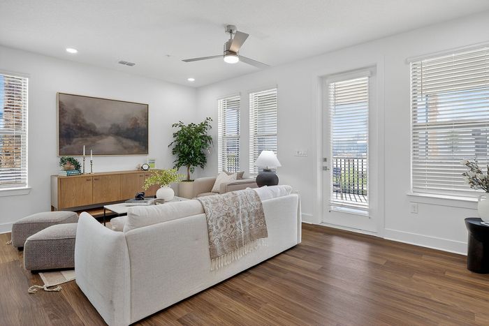 Bright and modern living room showcasing elegant hardwood floors, cozy seating, and abundant natural light through large windows.