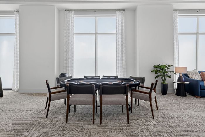 Elegant lounge area with a poker table, stylish seating, and large windows offering ample natural light.
