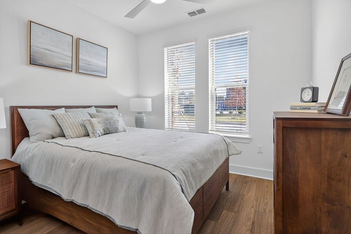 Charming bedroom with elegant decor featuring a cozy bed, stylish wooden furniture, and bright natural light through large windows.