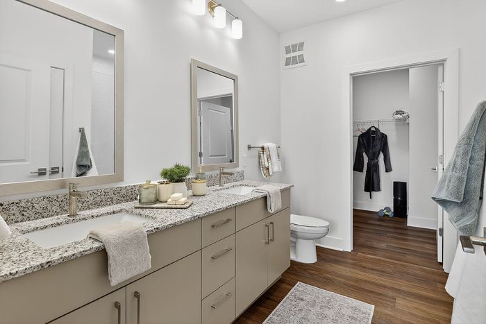 Modern bathroom with granite countertops, dual sinks, and sleek storage. Inviting walk-in closet and elegant wooden flooring.