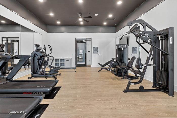 Modern gym with state-of-the-art fitness equipment including treadmills, ellipticals, and strength machines on elegant wood flooring, perfect for an invigorating workout.