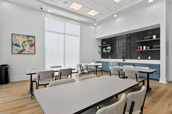 Bright and modern community room with sleek tables, contemporary art, and a chic kitchenette, perfect for gatherings.