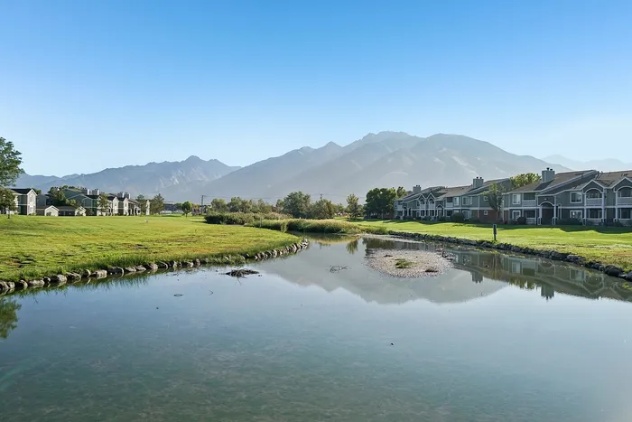 Scenic view of beautiful lakeside apartments with mountain backdrop and lush green lawns.