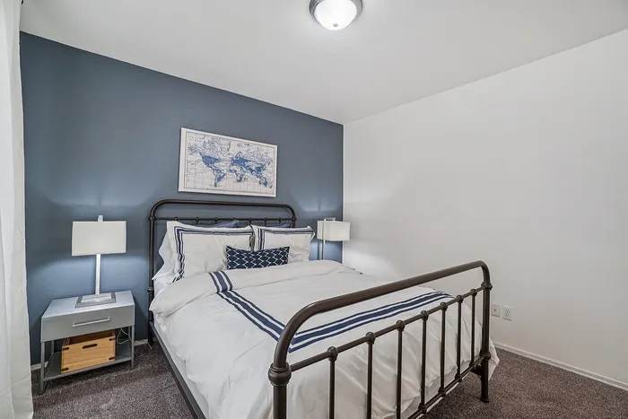 Cozy bedroom with a sleek metal bed frame, elegant white and blue bedding, and stylish map artwork on a soothing blue accent wall.