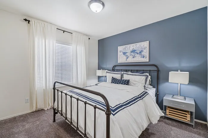 Charming bedroom with elegant metal bed frame, cozy blue accent wall, and bright natural light through sheer curtains.