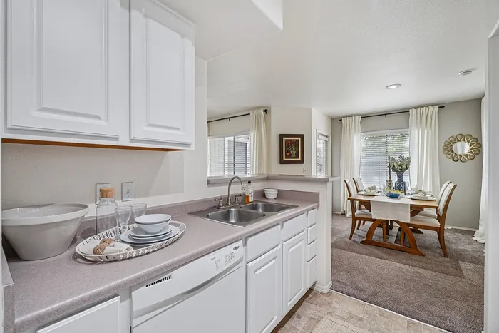 Bright kitchen with modern white cabinetry and adjoining elegant dining area, showcasing natural light and tasteful decor.