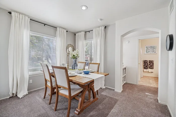Elegant dining room with a cozy atmosphere, featuring a wooden table set for four with fresh flowers and abundant natural light from large windows.