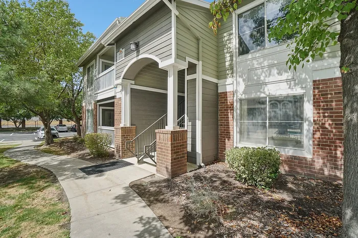 Charming apartment exterior with brick and siding, set in lush greenery and inviting pathway entrance.