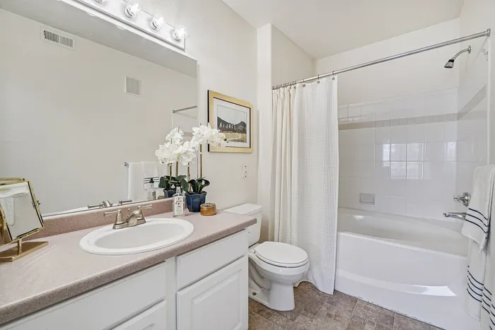 Bright and elegant bathroom featuring a large mirror, plush white vanity, and cozy shower-tub combo, accented by fresh orchids and modern lighting.