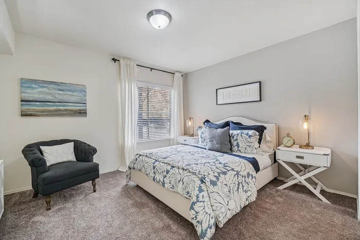 Inviting bedroom with chic decor, featuring a plush bed with floral bedding, elegant nightstands, and a cozy armchair by the window.