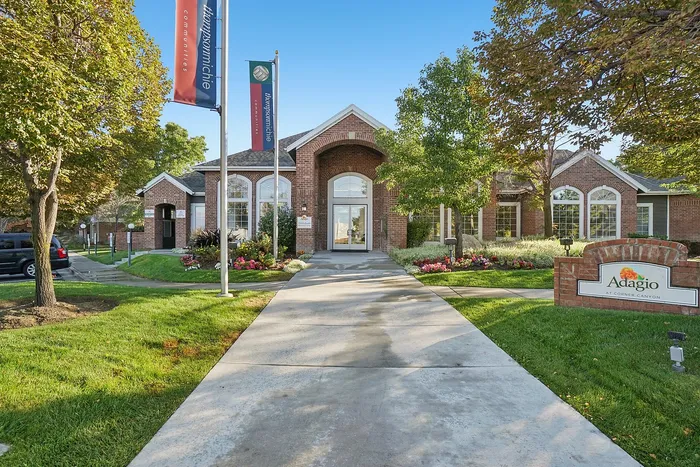 Charming brick apartment complex entrance surrounded by vibrant flowers and lush greenery, showcasing community elegance and tranquility.