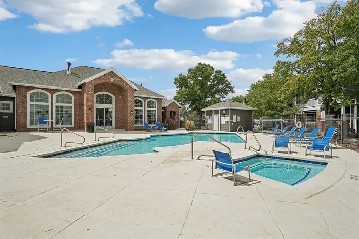 Inviting pool area with stylish lounge chairs and charming brick clubhouse under a bright blue sky.
