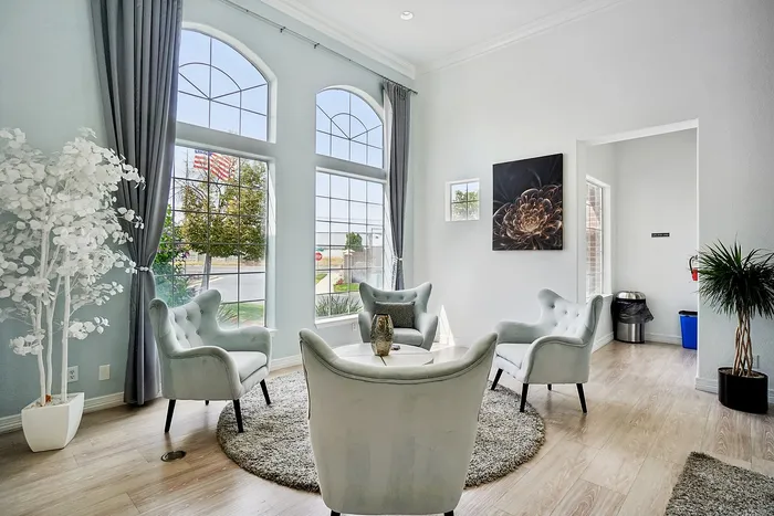 Elegant living room with tall arched windows, stylish armchairs, and a chic round table, illuminated by natural light.