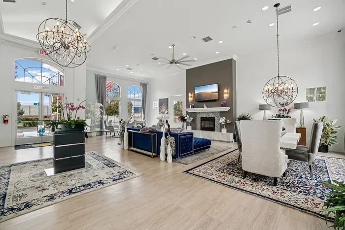 Elegant apartment living room with modern chandeliers, plush seating, and a cozy fireplace, framed by large sunny windows and stylish decor.
