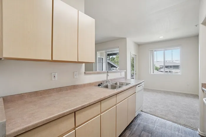 Bright and welcoming kitchen with modern cabinetry, dual sink, and expansive counters overlooking a sunlit living space.