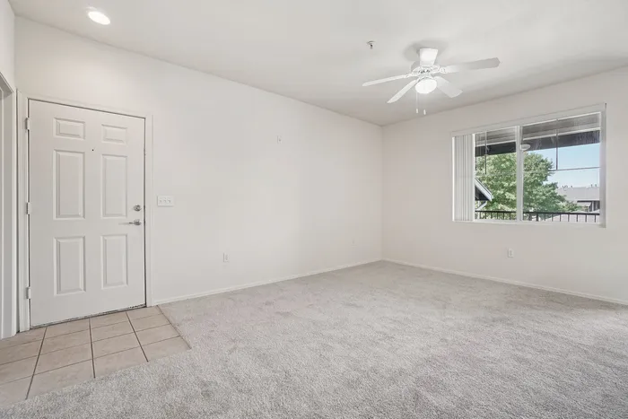 Bright and airy living room with plush carpeting, ceiling fan, and large window offering a scenic view, creating a welcoming atmosphere.