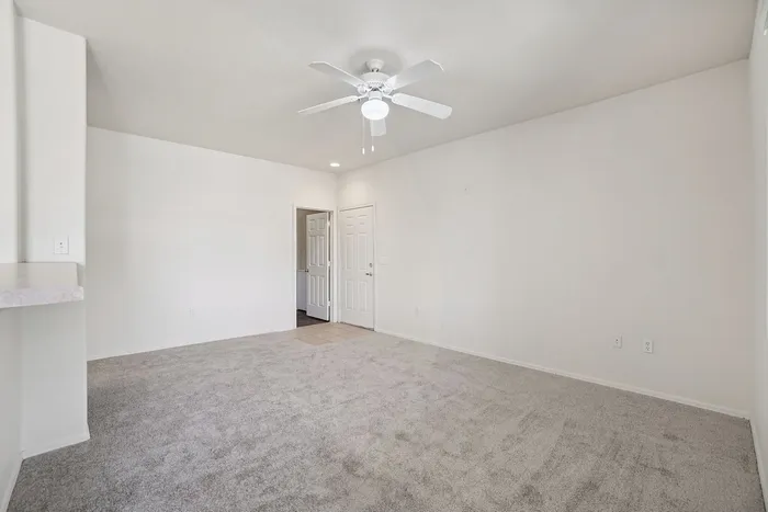 Bright, inviting living space with plush carpet, neutral walls, and a modern ceiling fan, perfect for cozy enjoyment.