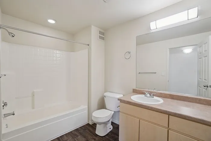 Contemporary bathroom with elegant recessed lighting, large mirror, and sleek white bathtub on polished dark wood flooring.