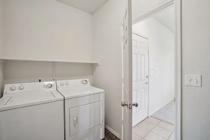 Bright and convenient laundry room featuring top-load washer and dryer with easy access to adjacent hallway.
